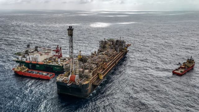 Plataforma de petróleo tipo FPSO no mar, ladeada por embarcações de apoio