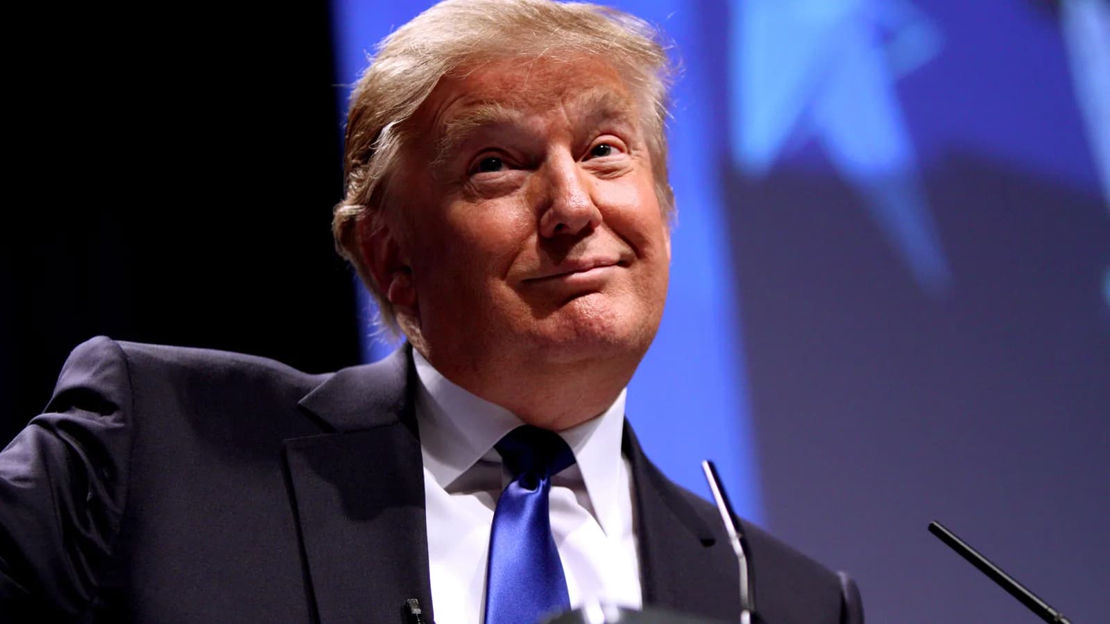 Donald Trump discursa em evento político, de terno escuro e gravata azul