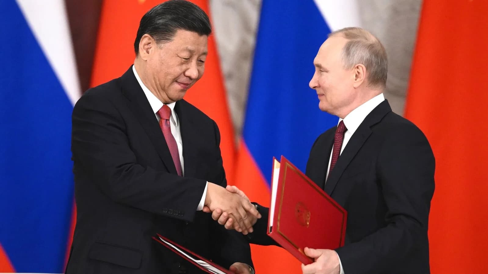 Vladimir Putin e Xi Jinping apertam as mãos diante das bandeiras da Rússia e da China