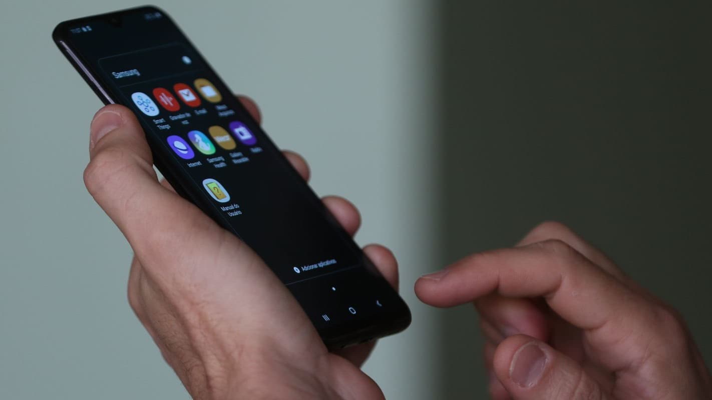 Mãos de uma pessoa segurando e mexendo em um smartphone Android com tela de aplicativos acesa