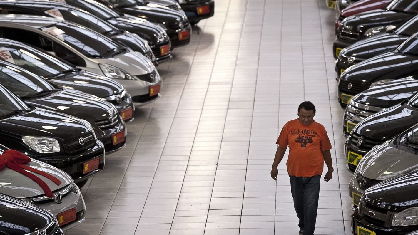 Consumidor caminha entre fileiras de carros em pátio de revendedora de veículos