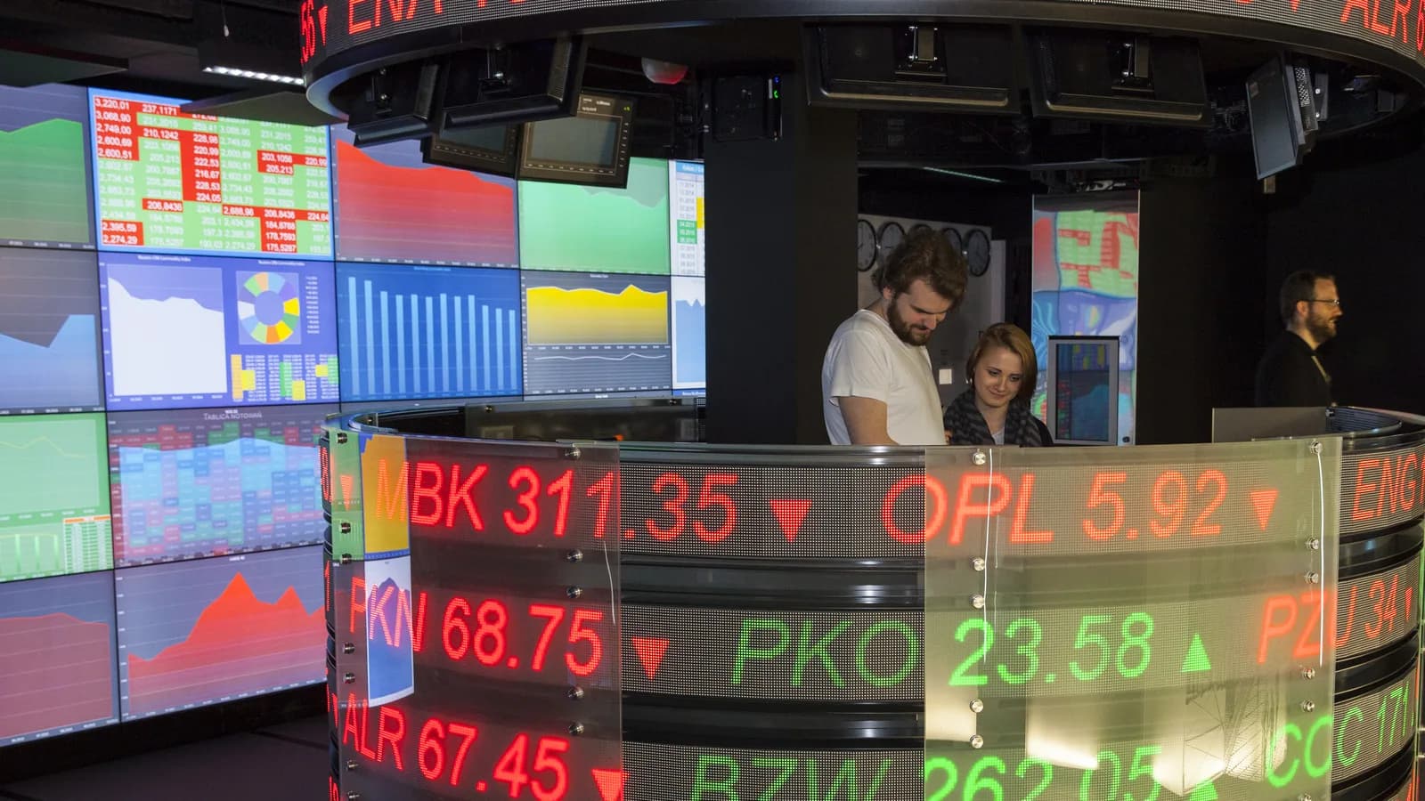 Painel de cotações em mercado financeiro, com operadores acompanhando preços de ações