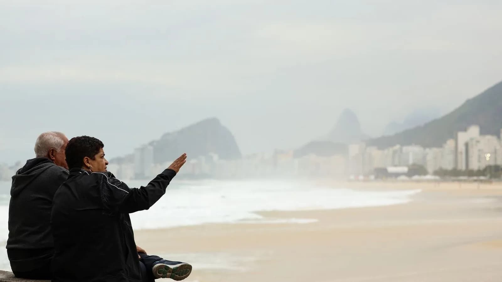 Casal agasalhado observa o mar em dia frio e nublado em Copacabana, no Rio de Janeiro