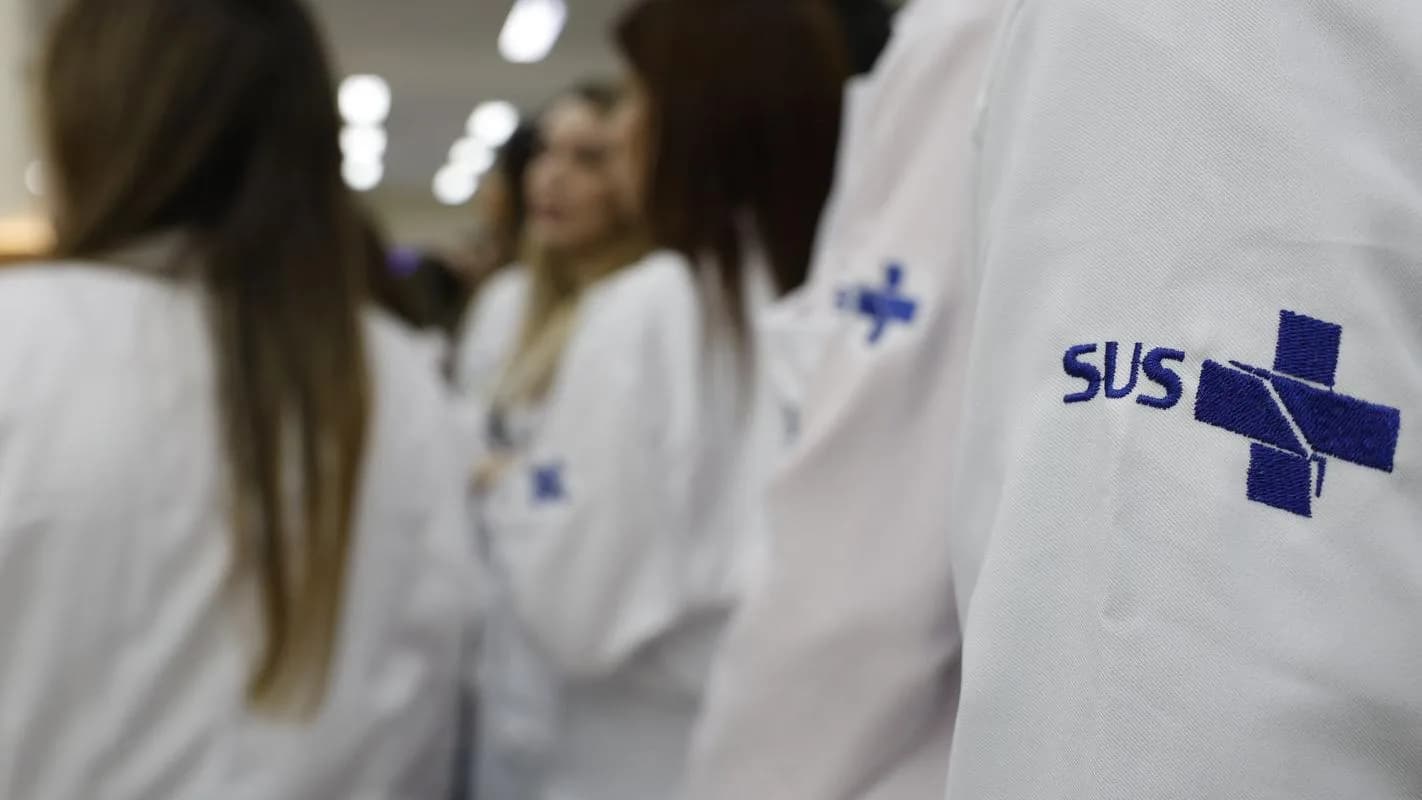 Profissionais de saúde com jalecos bordados com o logo do SUS