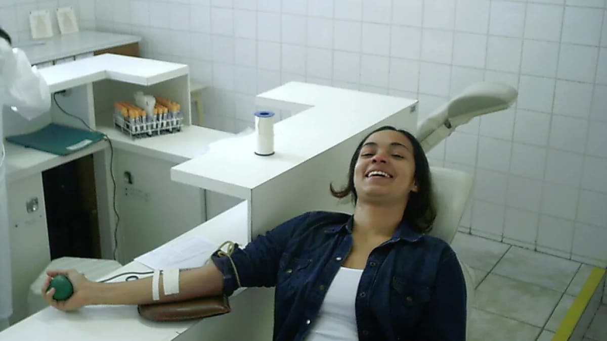 Mulher sorri enquanto doa sangue em hemocentro, com cateter no braço