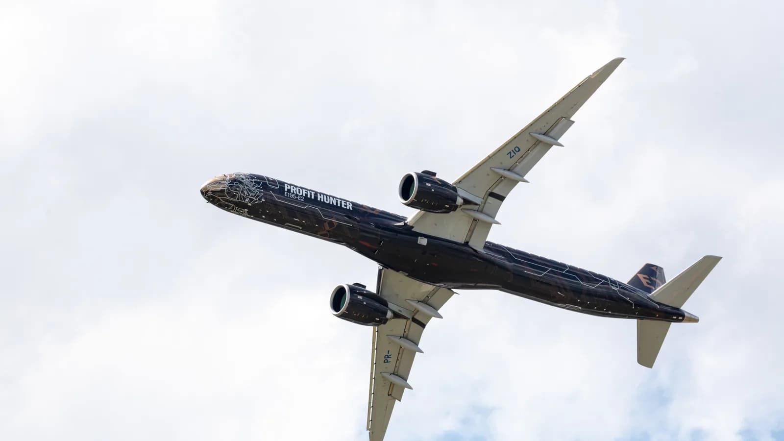 Avião Embraer E195-E2 em voo, visto de baixo contra o céu com nuvens
