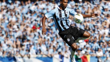 Jogador do Grêmio disputa bola no ar durante clássico Gre-Nal, com torcida ao fundo, foto de arquivo