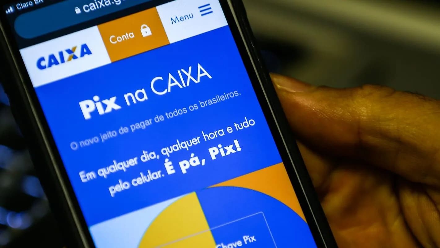 Mão segura celular com a tela do aplicativo do Pix na Caixa, sistema de pagamento instantâneo brasileiro