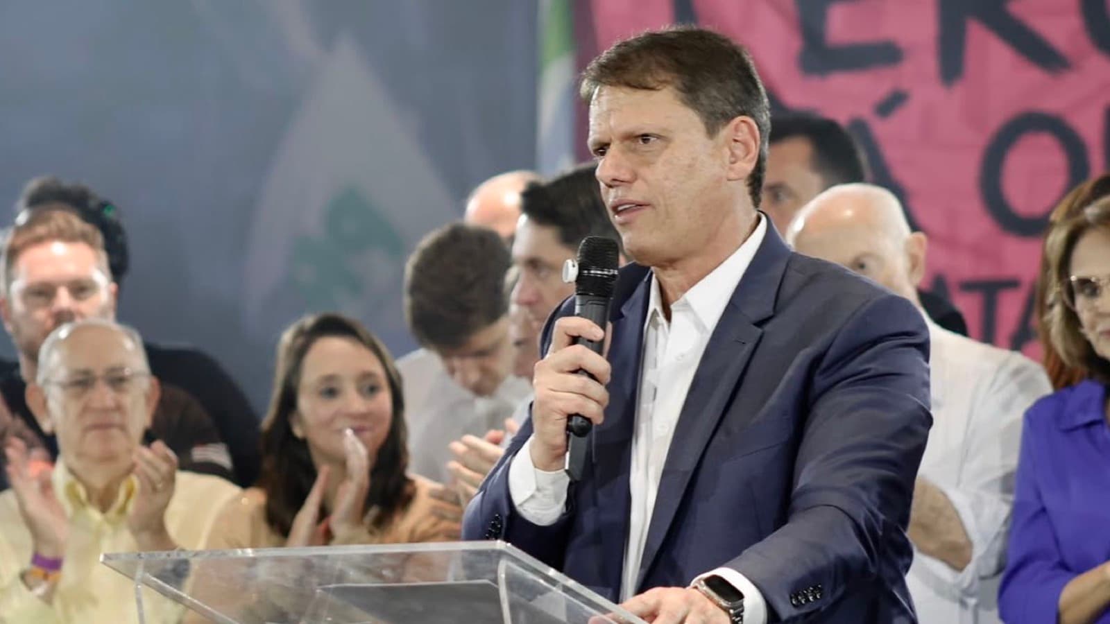 Tarcísio de Freitas fala ao microfone atrás de um púlpito de acrílico durante a convenção do Republicanos, com apoiadores aplaudindo ao fundo