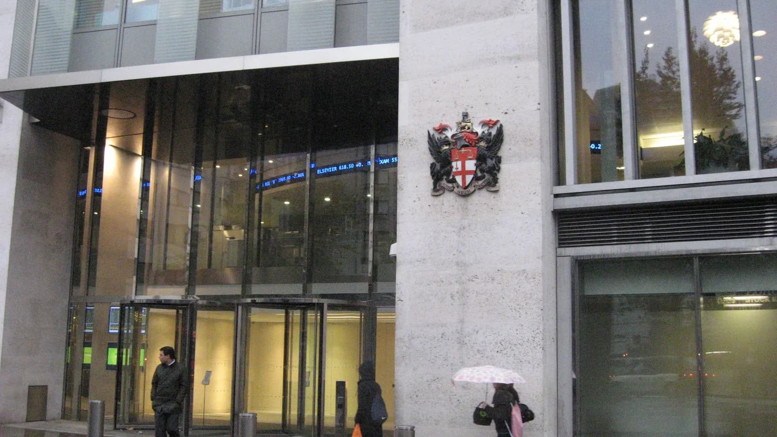 Entrada do prédio da Bolsa de Londres, com pessoas passando pela porta giratória