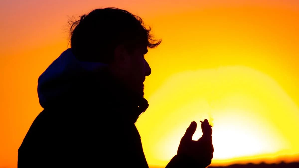 Silhueta de pessoa fumando um cigarro ao entardecer