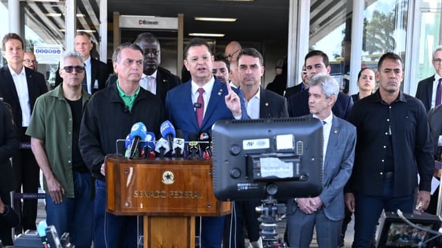 Jair Bolsonaro, de camisa verde, e o senador Flávio Bolsonaro atrás de um púlpito do Senado Federal durante entrevista coletiva, cercados por parlamentares e microfones da imprensa, em imagem de arquivo de julho de 2025