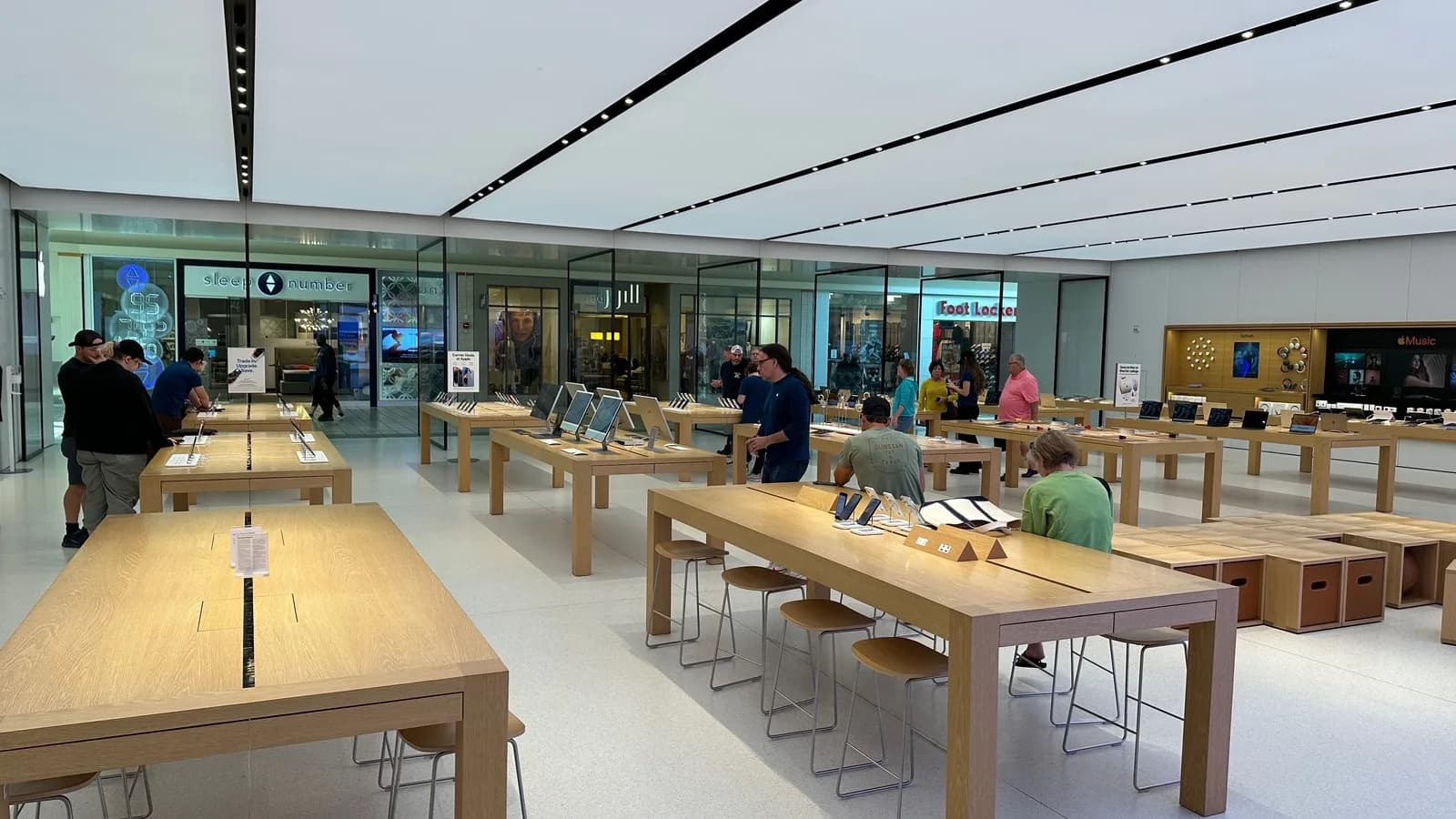 Clientes observam produtos em mesas de madeira dentro de uma loja da Apple