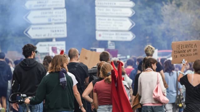 Manifestantes de costas em protesto estudantil nas ruas de Bayonne, na França, com fumaça ao fundo