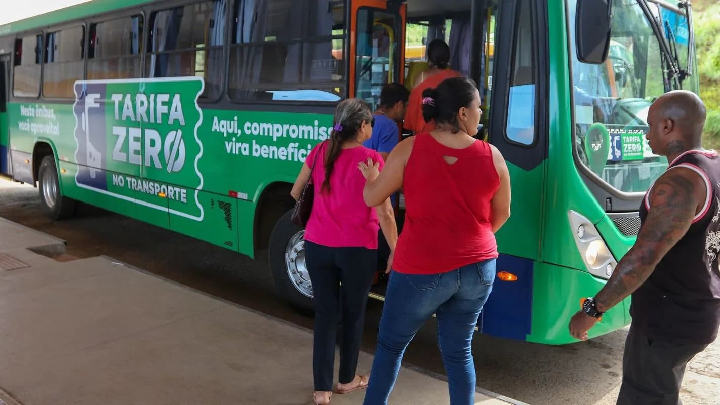 Passageiros embarcam em ônibus com adesivo "Tarifa Zero" em via urbana