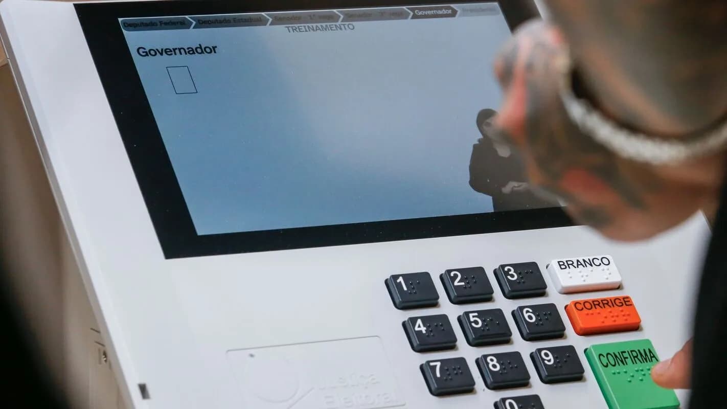 Mão de eleitor digita em urna eletrônica na tela de votação para governador