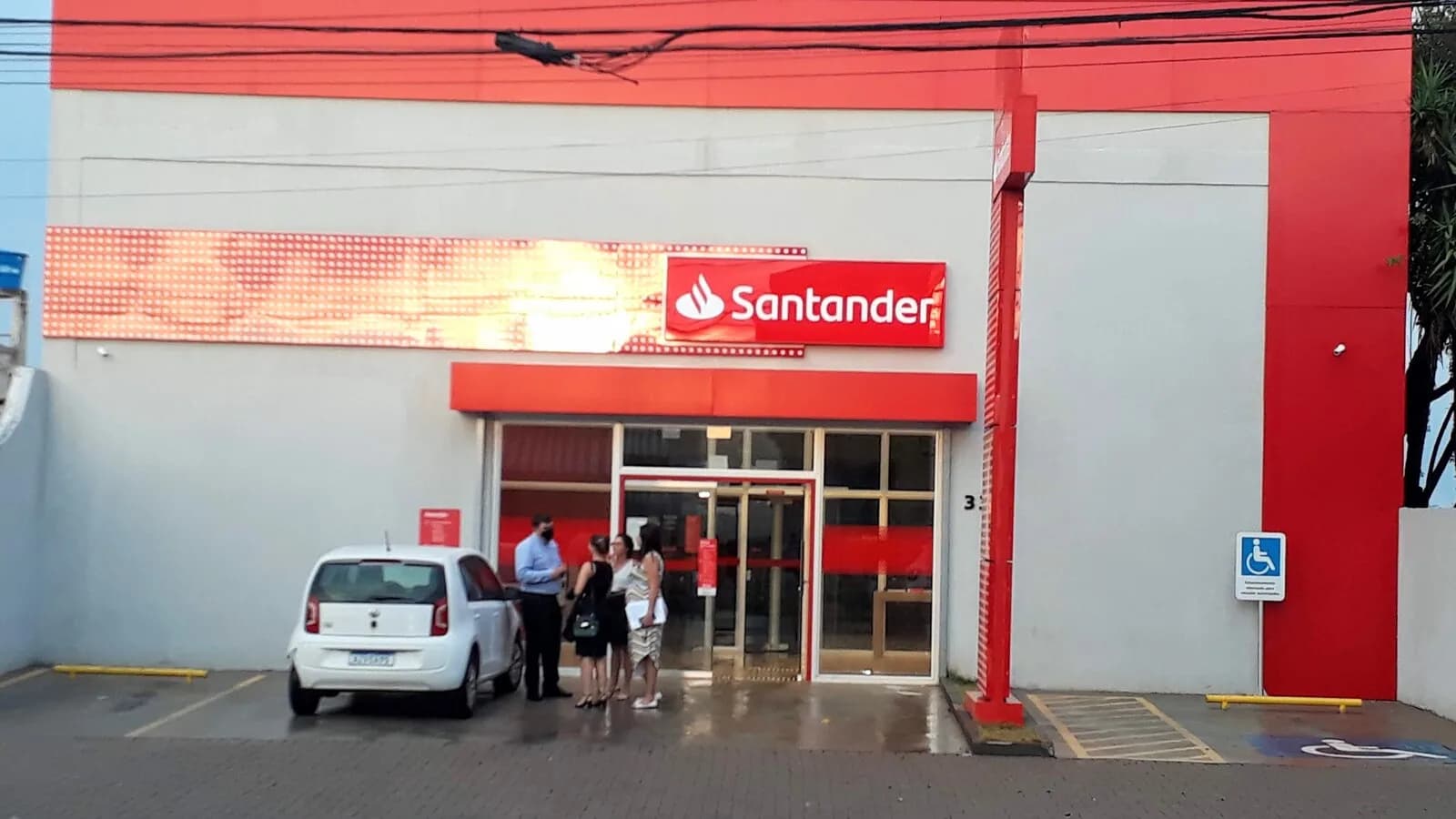 Fachada de agência do Santander com clientes em frente