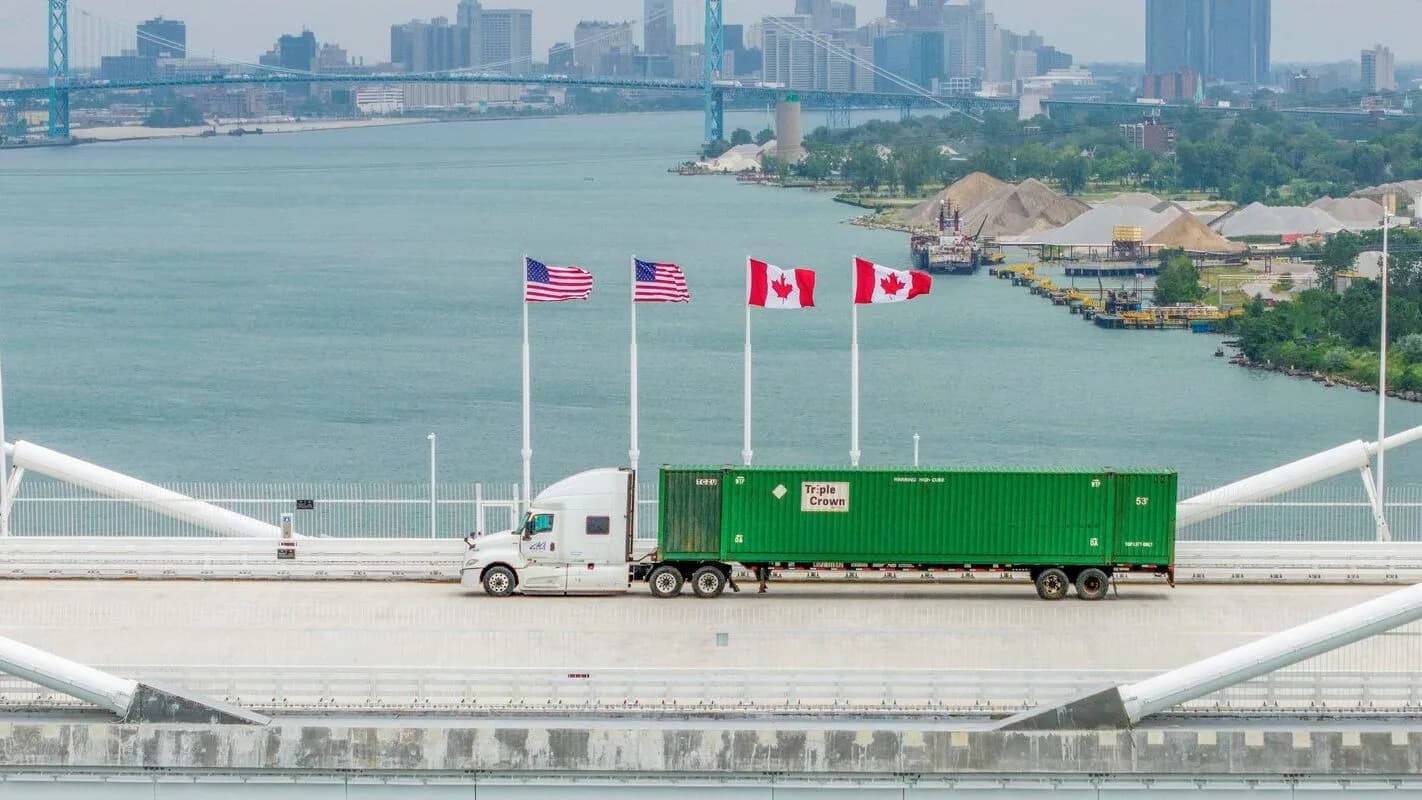 Caminhão de carga cruza ponte de fronteira entre Estados Unidos e Canadá, com bandeiras dos dois países