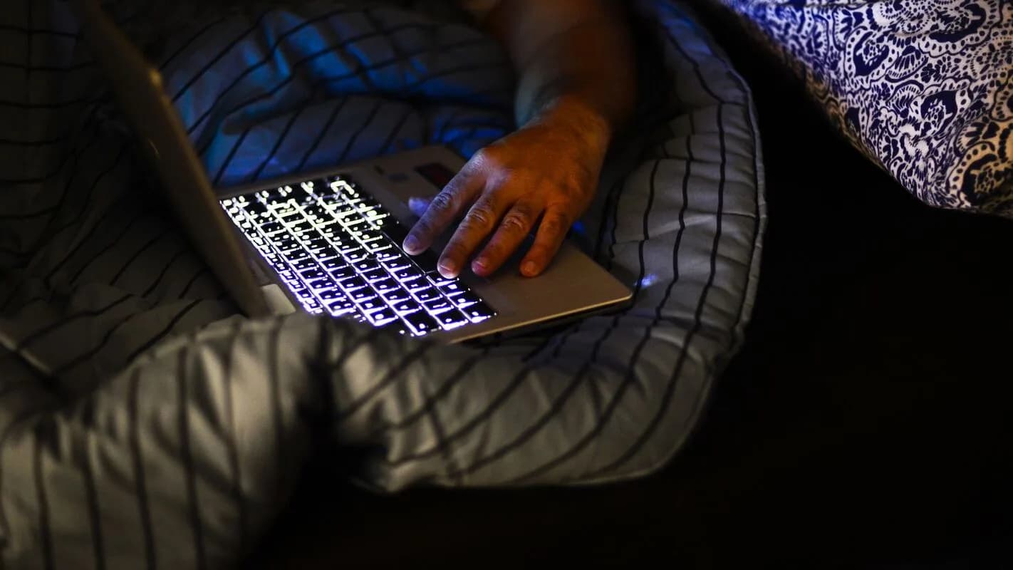 Pessoa deitada na cama à noite mexendo no celular iluminado, foto de arquivo