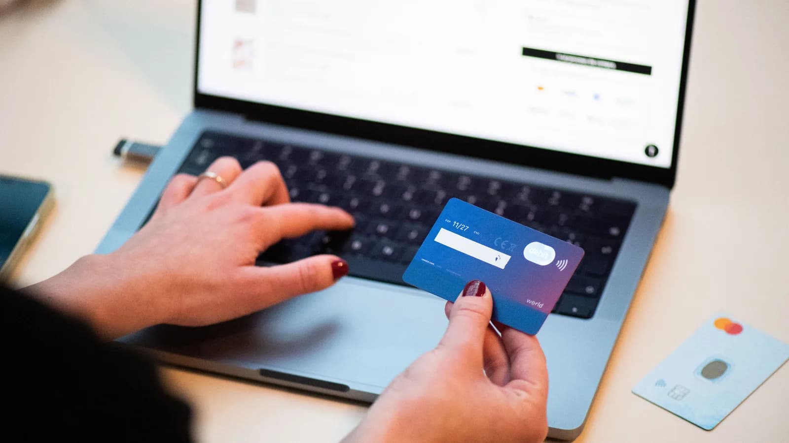 Pessoa faz compra online segurando cartão bancário em frente a um notebook