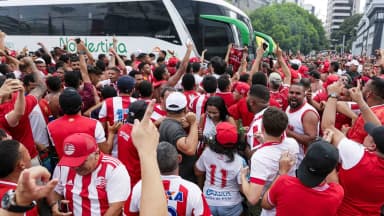 Torcedores do Náutico vestindo camisas rubro-brancas aglomerados em frente a ônibus do clube