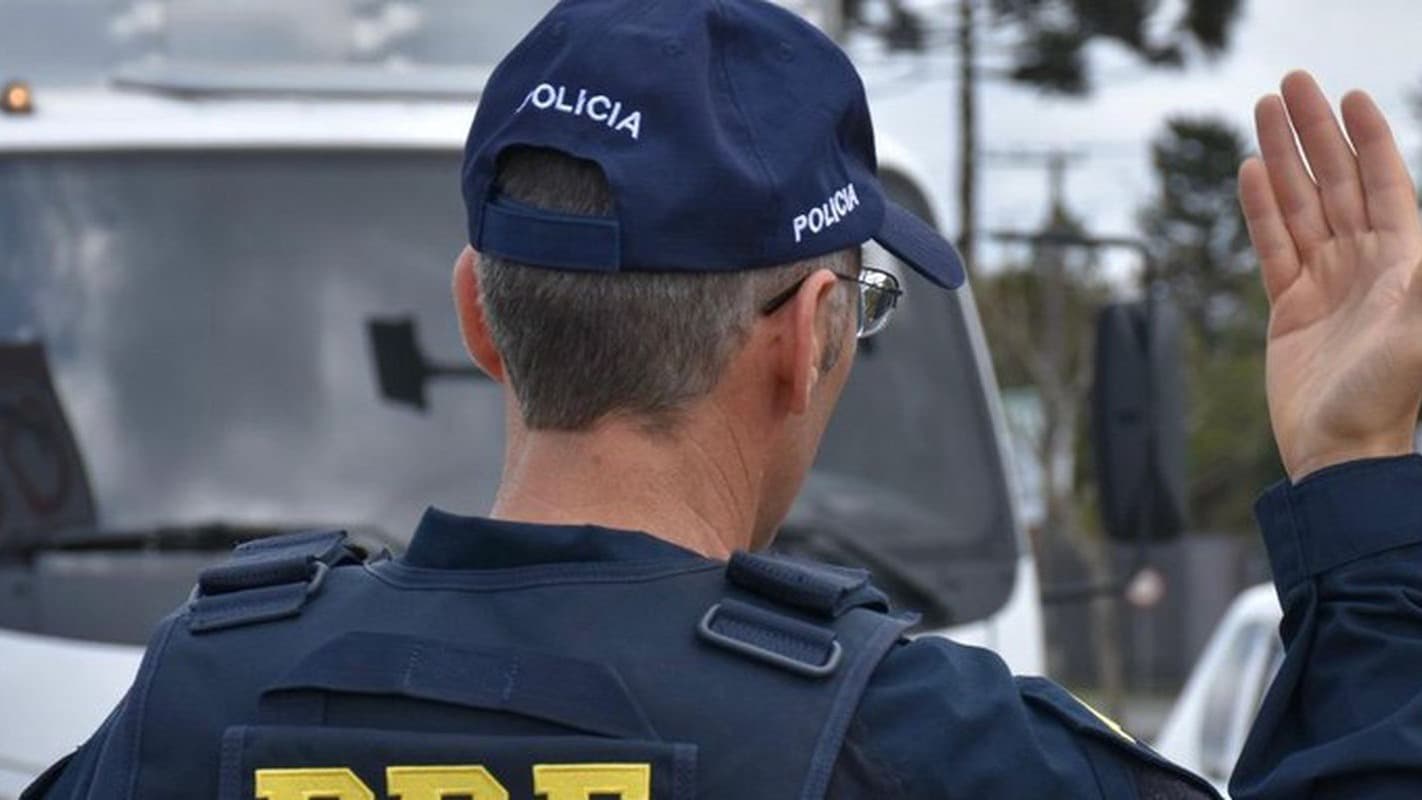 Agente da Polícia Rodoviária Federal de costas, fazendo sinal com a mão em fiscalização de rotina em rodovia (foto de arquivo)