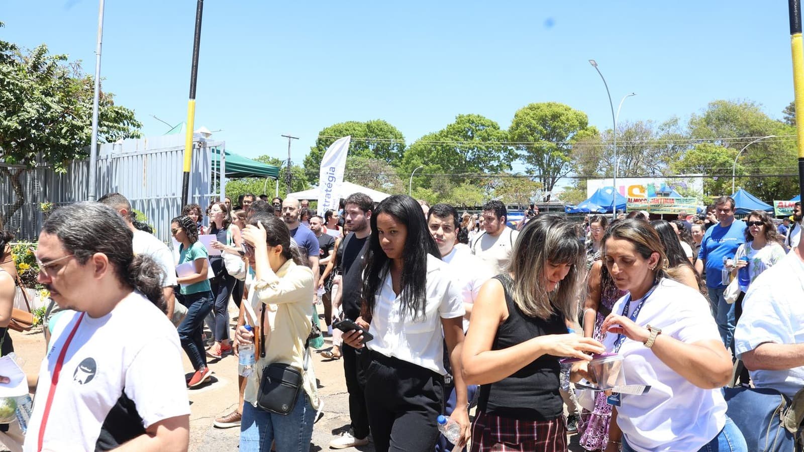 Grupo de estudantes adultos caminha em área externa de um local de provas, em dia de sol; imagem de arquivo