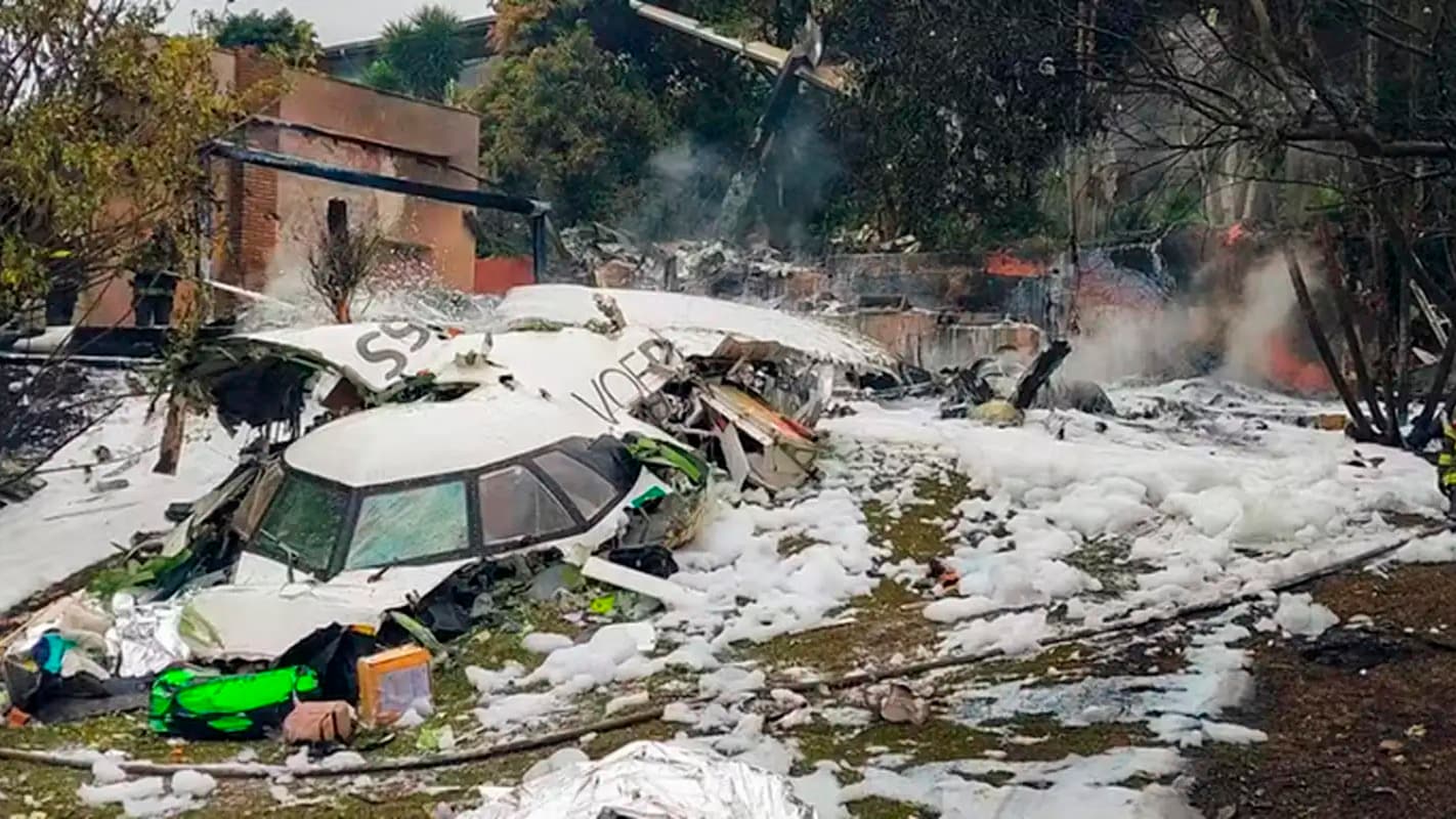 Destroços do avião da Voepass cobertos de espuma de combate a incêndio, com bombeiros ao fundo, em Vinhedo (SP)