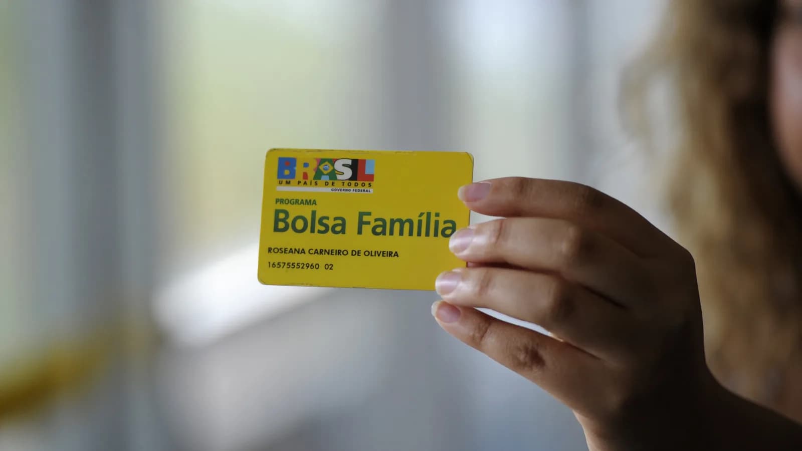 Mulher segura cartão do Programa Bolsa Família