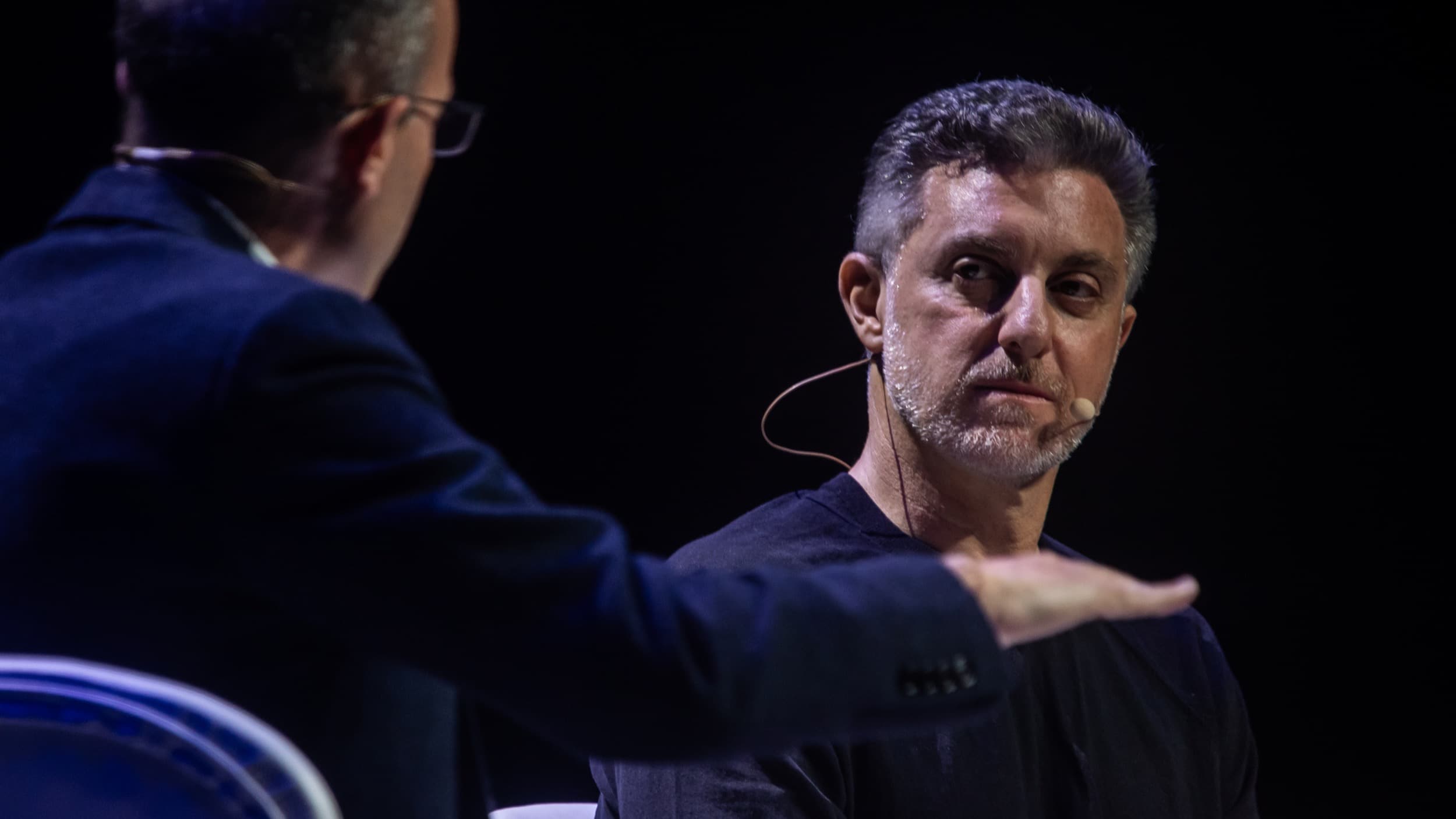 Luciano Huck durante entrevista em evento, usando microfone de lapela