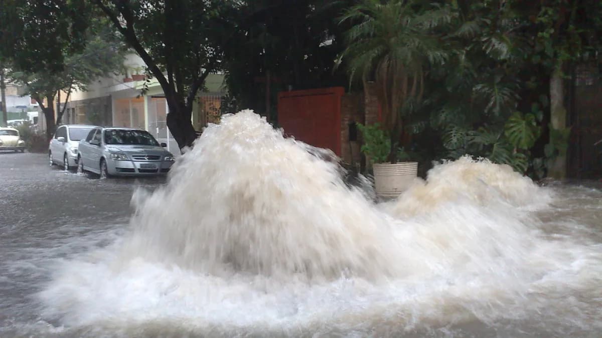 Água forma grandes poças e corre com força em rua alagada de São Paulo durante chuva