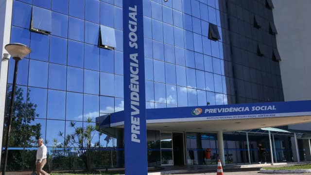 Fachada da sede do INSS em Brasília, com pedestre passando em frente