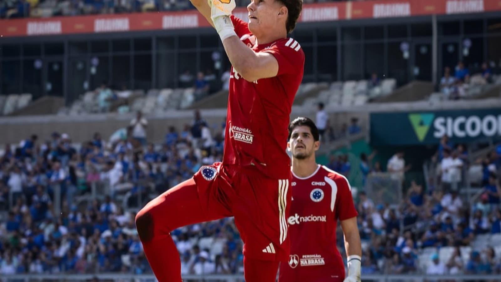 Goleiro do Cruzeiro, de uniforme vermelho, espalma a bola durante jogo contra o Mirassol no Mineirão, com arquibancada lotada ao fundo