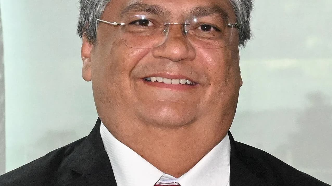 Retrato do ministro Flávio Dino, de terno escuro e óculos, sorrindo