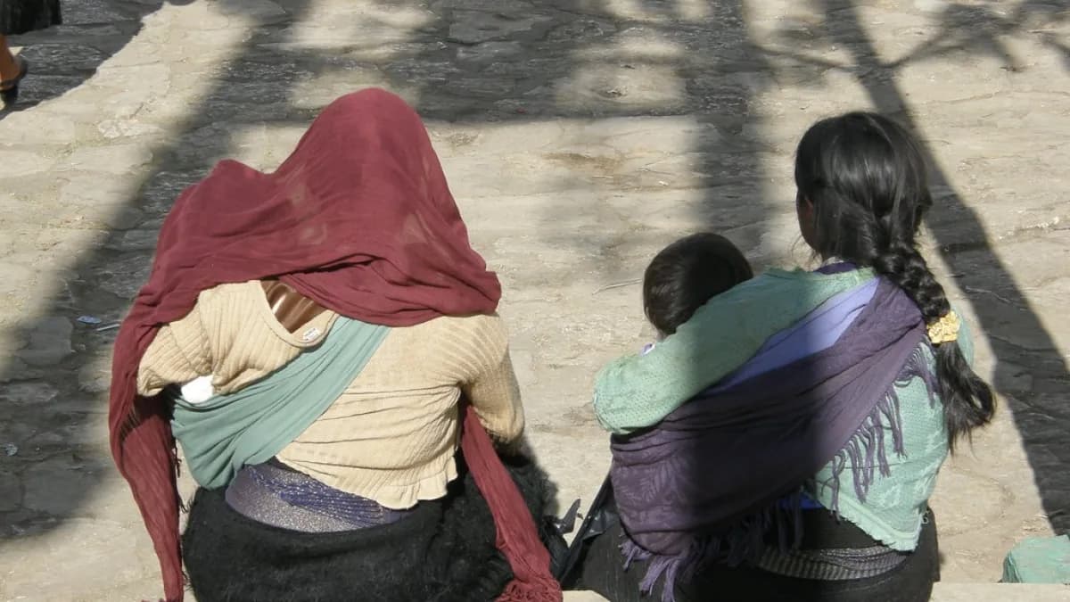 Mulheres indígenas sentadas, uma delas com criança no colo