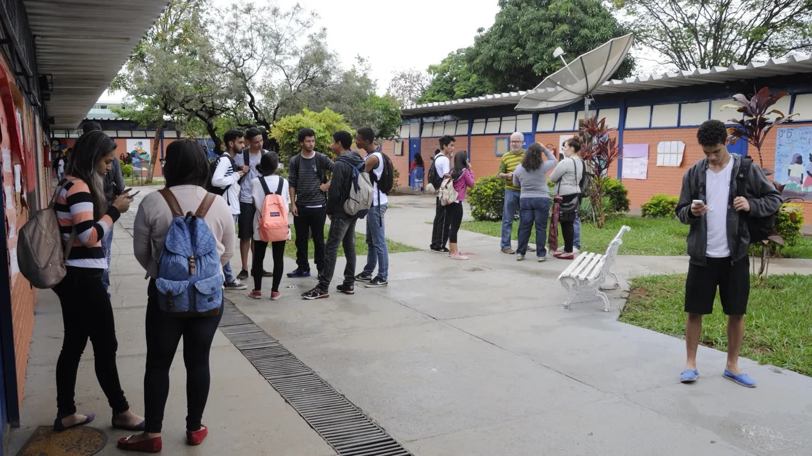 Estudantes em pátio de escola pública, mochilas nas costas