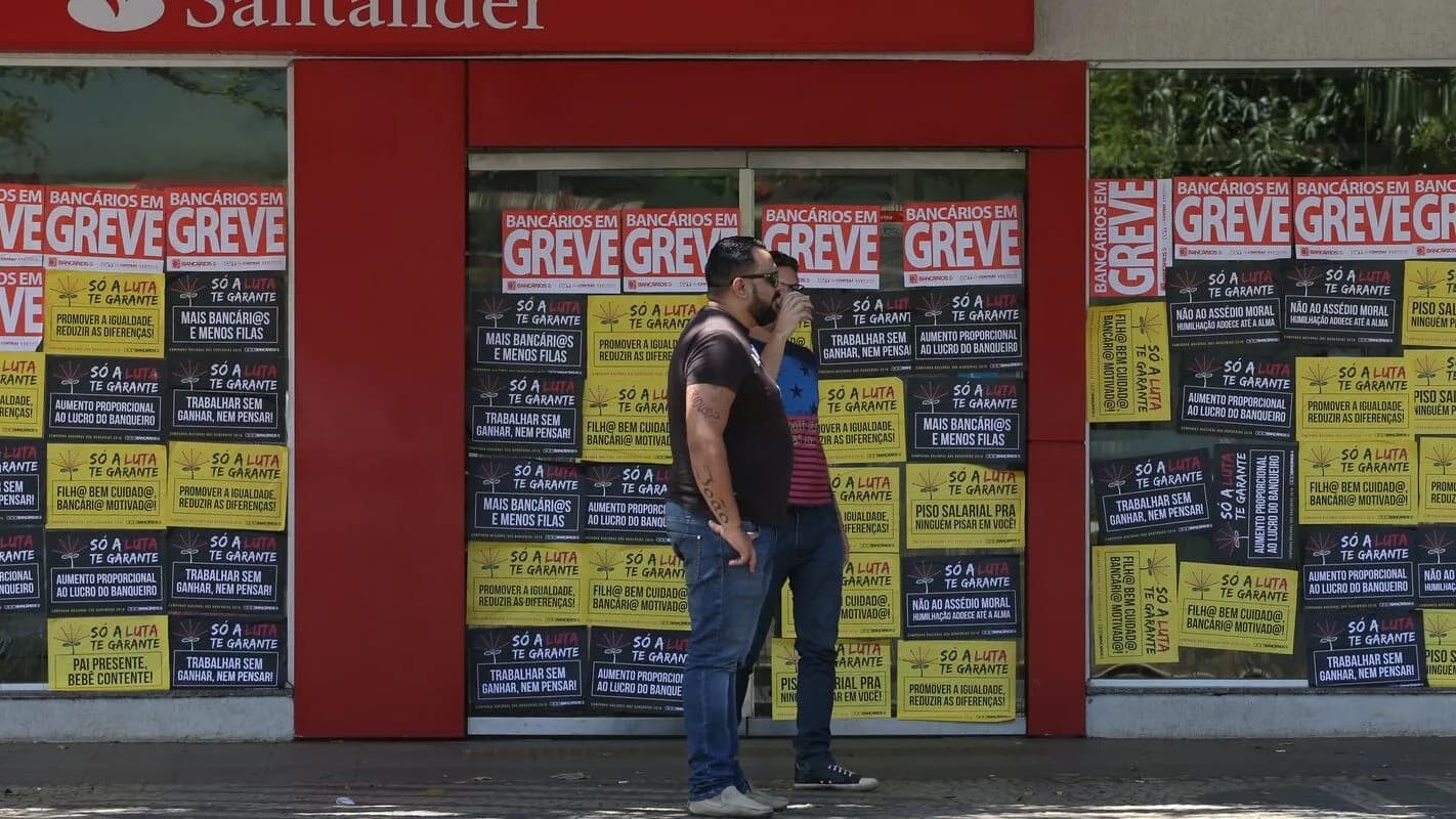 Homens passam em frente a agência bancária com cartazes de bancários em greve (foto de arquivo)