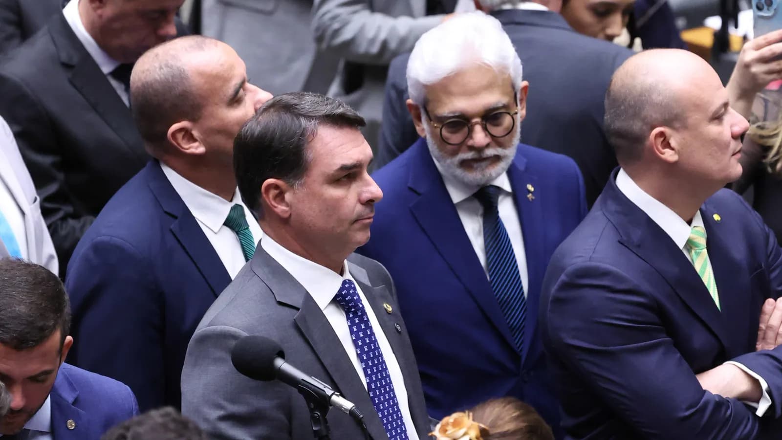 Flávio Bolsonaro fala ao microfone em plenário, cercado por parlamentares, em foto de arquivo