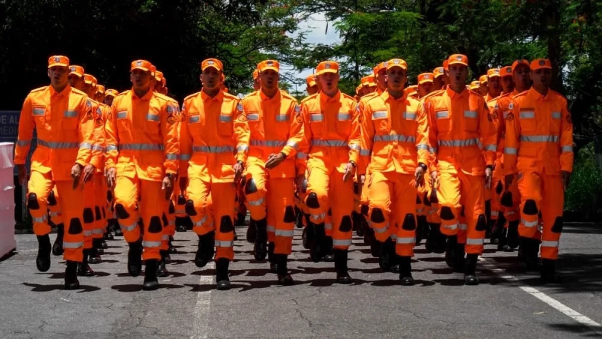 Fileira de soldados do Corpo de Bombeiros Militar de Minas Gerais, em uniforme laranja, marchando em formatura