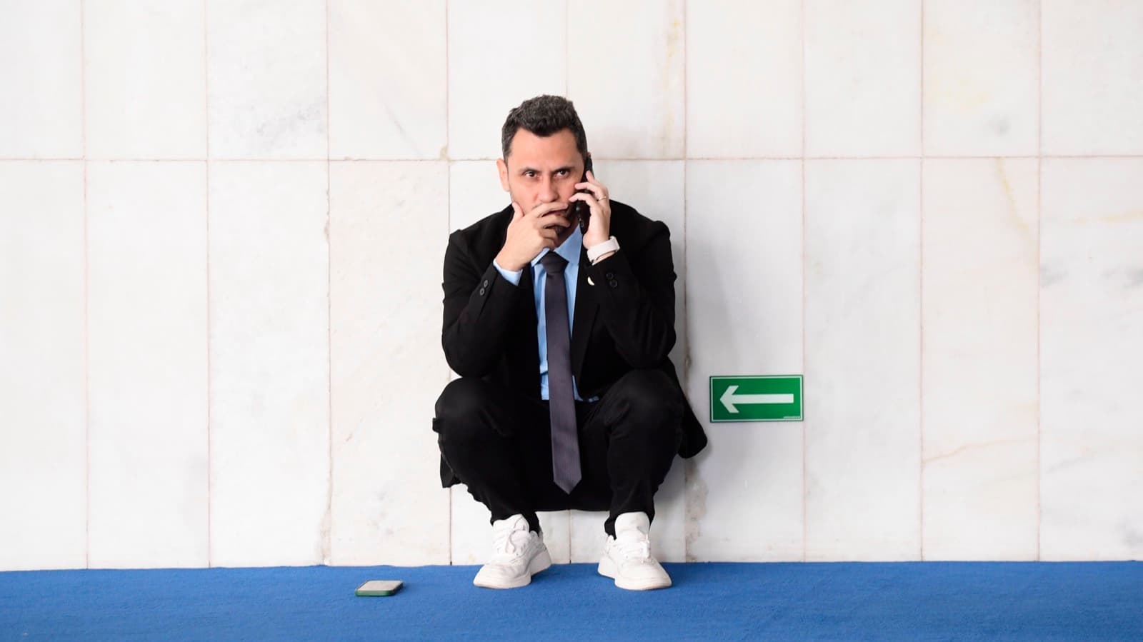 Senador Cleitinho Azevedo agachado ao telefone em corredor do Senado