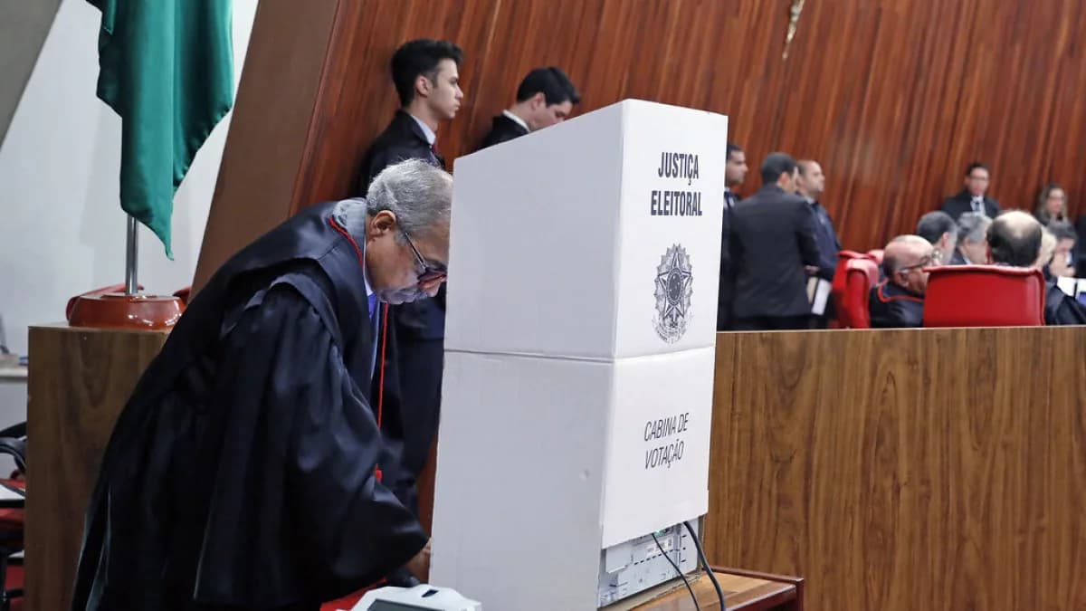 Autoridade vota em cabine da Justiça Eleitoral, com mesa de mesários ao fundo