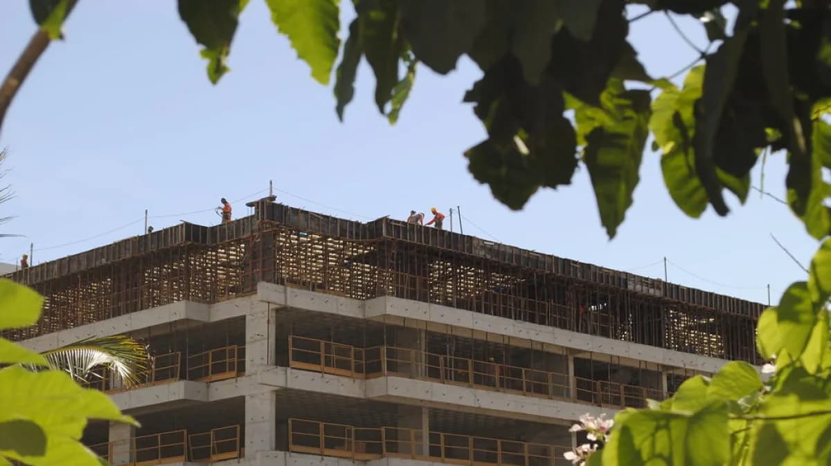 Trabalhadores em obra de prédio em construção, com estrutura de concreto e ferragens aparentes