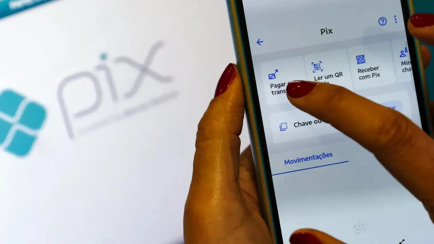 Mão com celular aberto no aplicativo do Pix, mostrando as opções de pagamento por QR Code