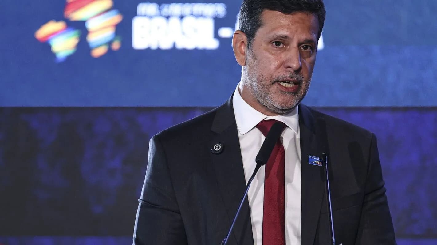 O senador Camilo Santana discursa em evento, com microfones à frente, vestindo terno escuro e gravata vermelha