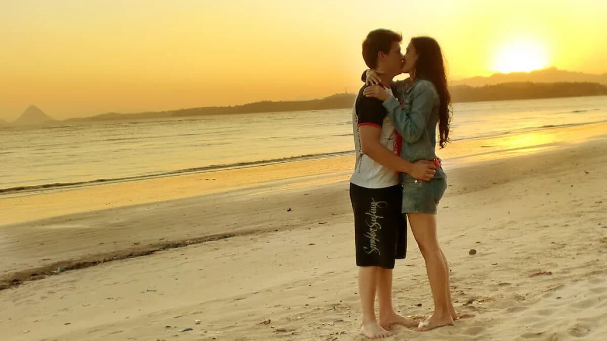 Casal se beija ao entardecer na praia, imagem ilustrativa sobre afeto e intimidade