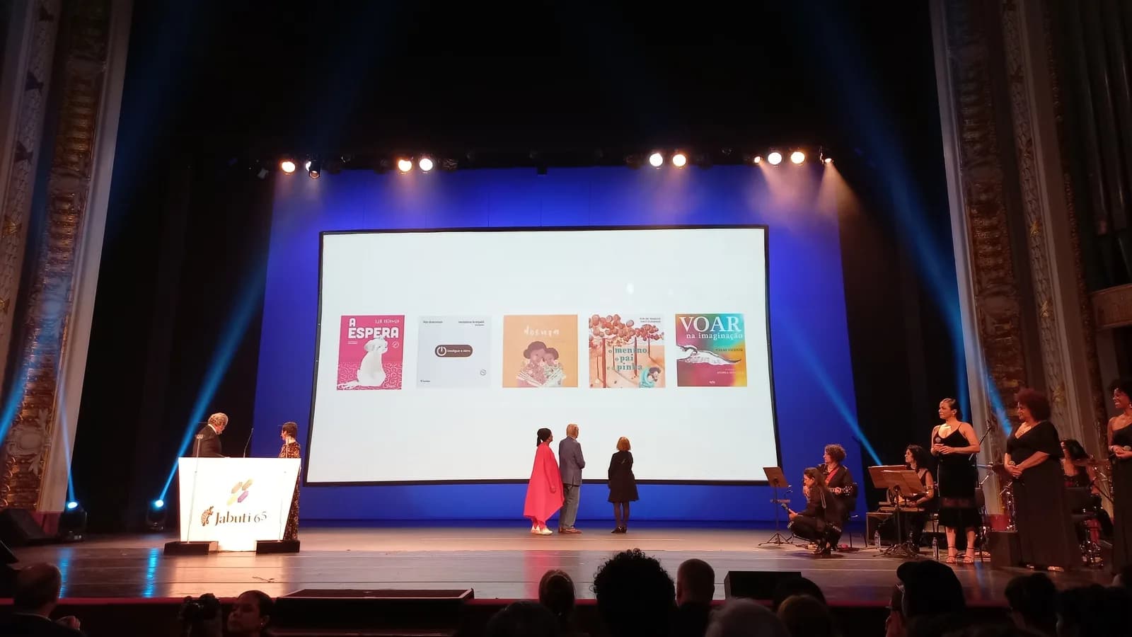 Palco de cerimônia do Prêmio Jabuti com plateia e telão exibindo capas de livros indicados